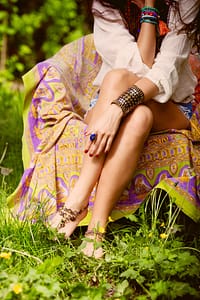 young barefoot woman sit in garden on armchair wearing boho style clothes focus on hand with ring and massive bracelet, outdoor day shoot